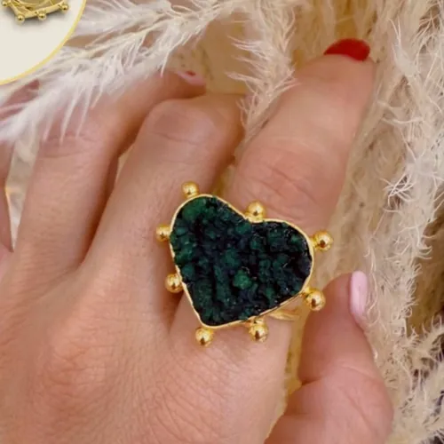 Ring with a heart-shaped raw emerald held by gold-tone claws, worn on the hand.