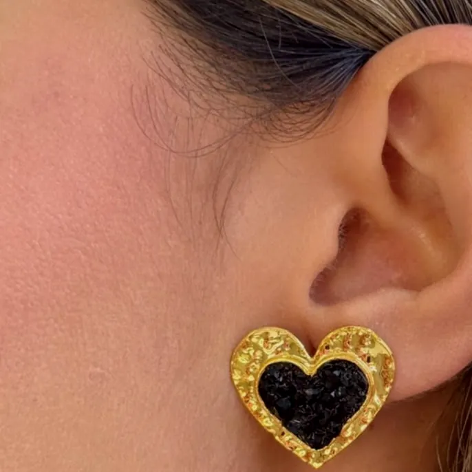 Black stone heart earring in a gold-tone frame, worn on the ear.