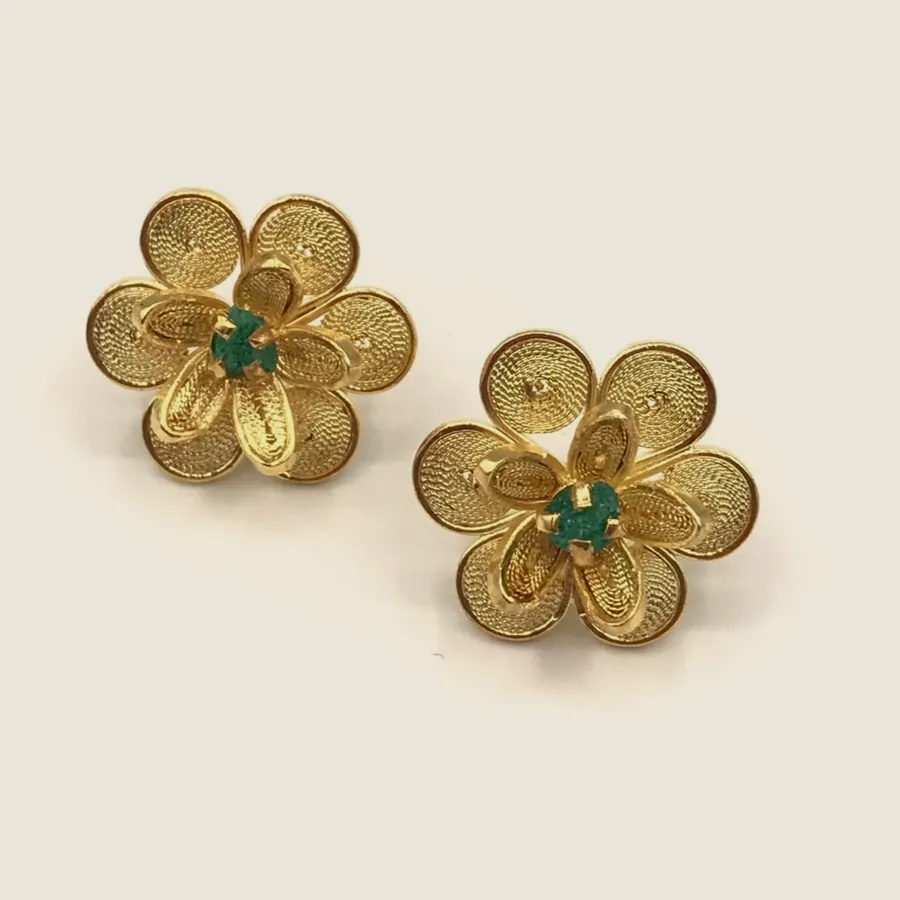 Gold-tone filigree earrings shaped as a five-petal flower with a raw emerald at the centre.