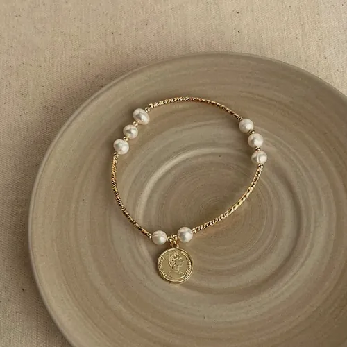 Bracelet of gold-tone beads and pearls with an engraved medallion hanging.