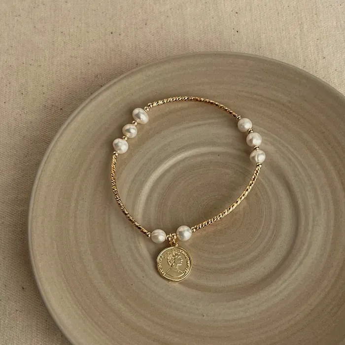 Bracelet of gold-tone beads and pearls with an engraved medallion hanging.