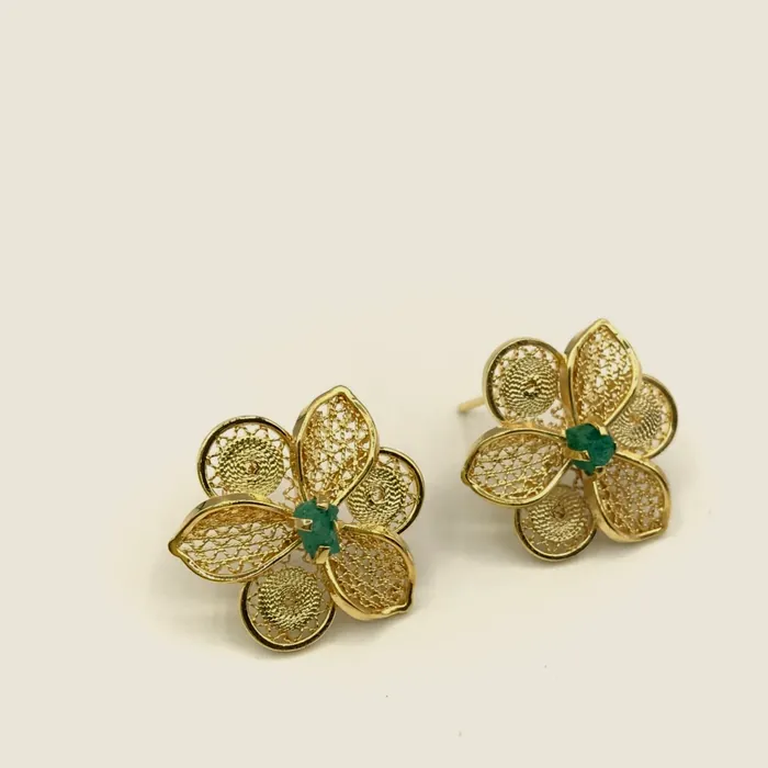 Gold-tone filigree earrings with four petals and a raw emerald at the centre.