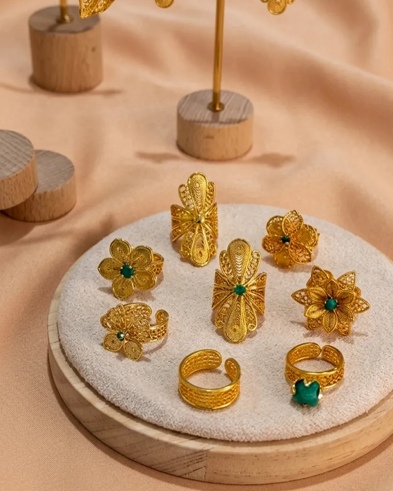 Gold filigree rings and earrings with green stones on peach fabric.