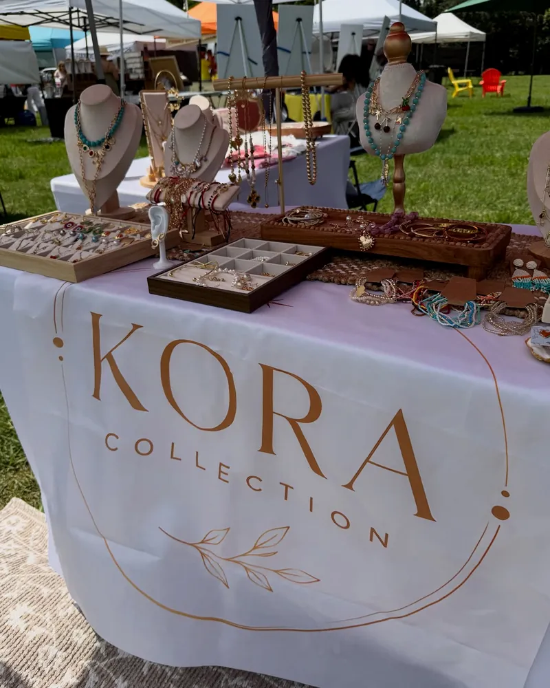 The KORA table at the open-air market, with busts and jewelry displays.