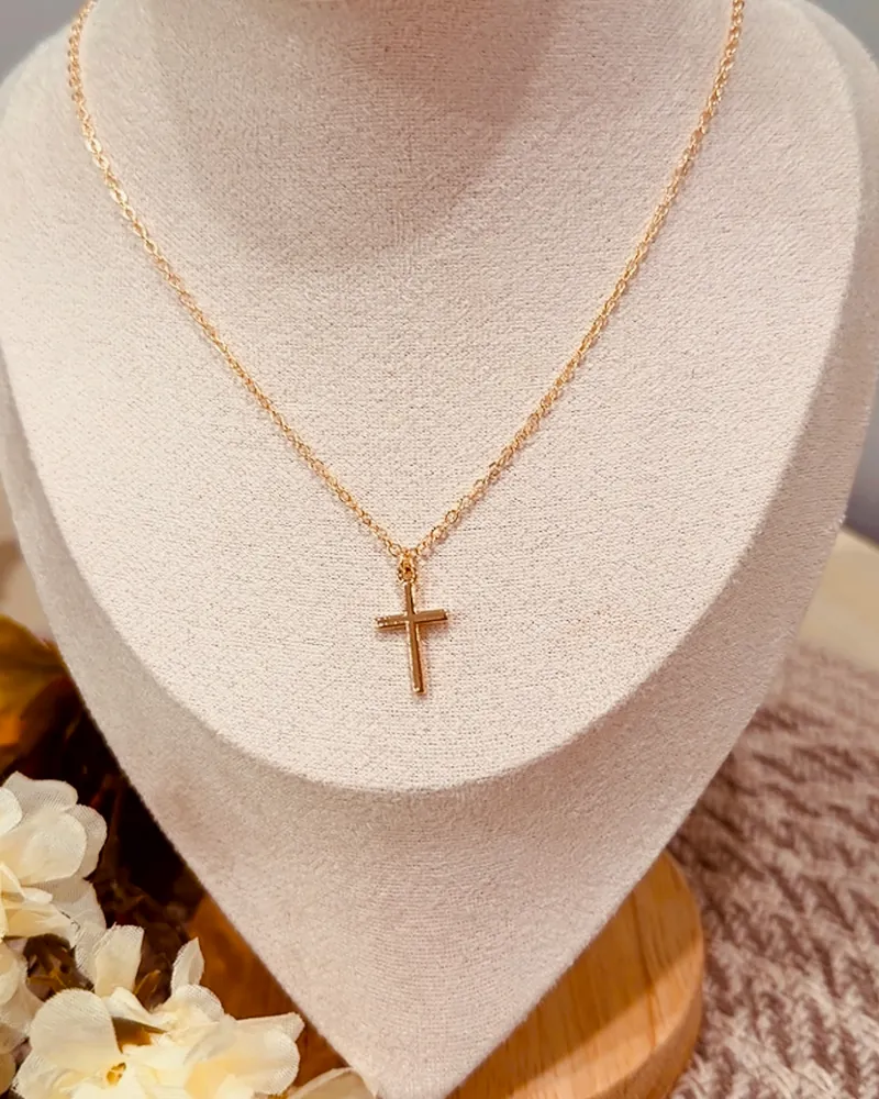 A gold necklace with a cross pendant on a cream velvet bust.