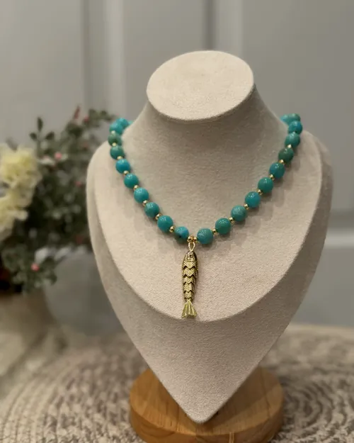 Turquoise necklace with gold pendant on a bust.