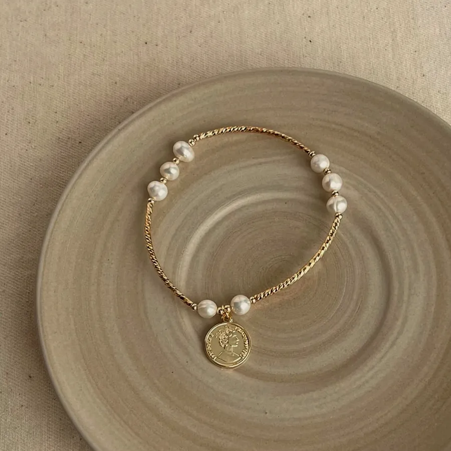 Pearl bracelet with a gold medal on a ceramic plate.