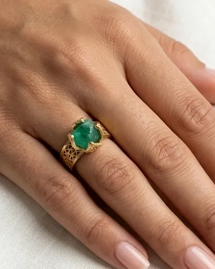A gold filigree ring with a green stone worn on the hand.